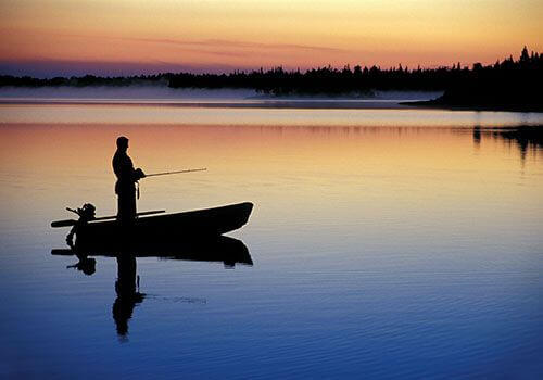 Fisherman on boat on calm waters at sunset